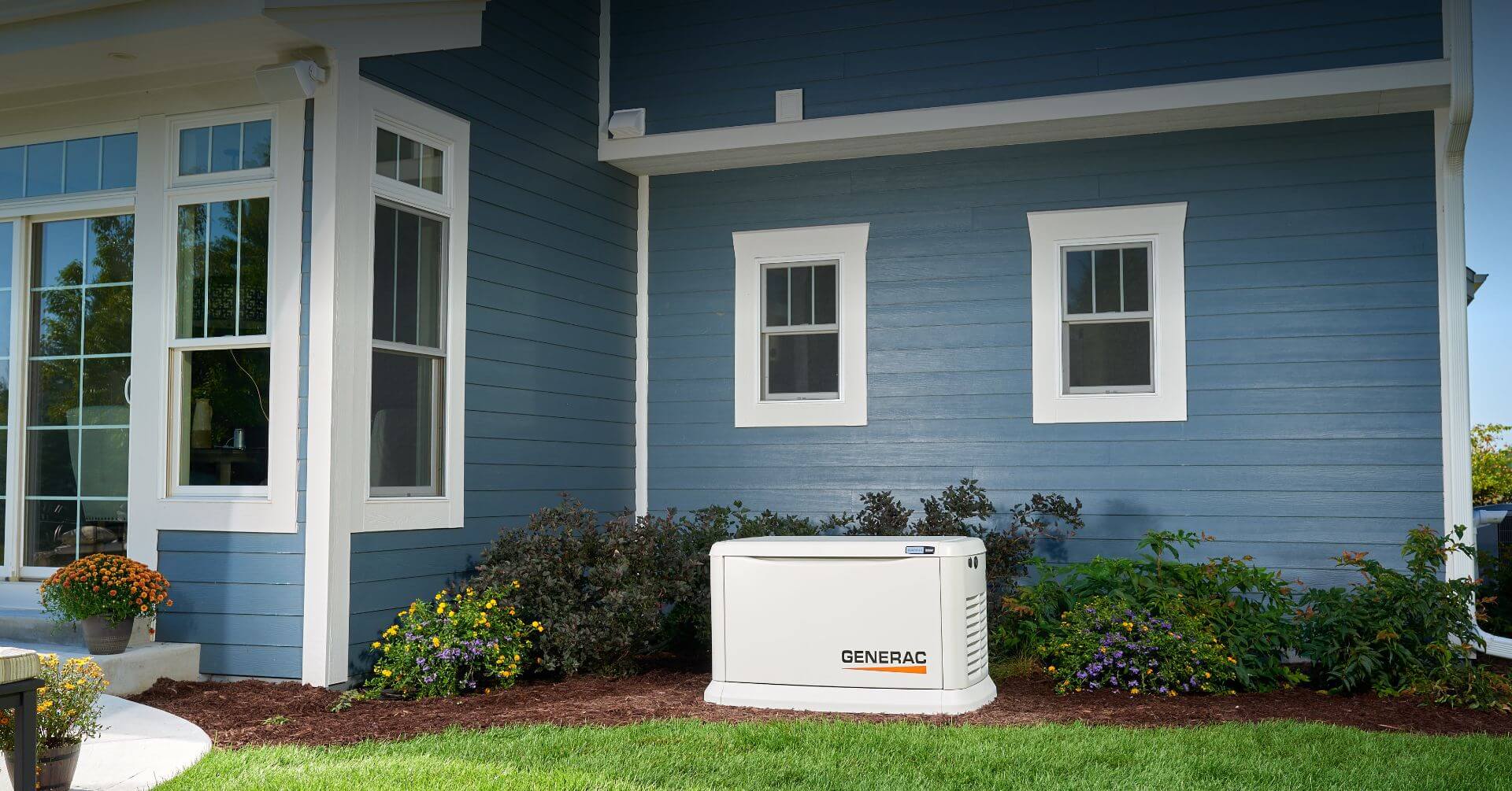 Generac residential generator sitting out side in the back of a house with blue siding